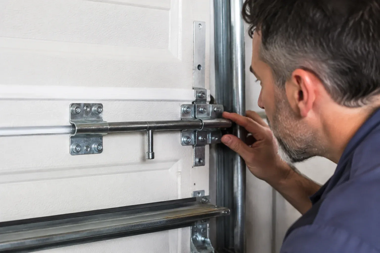 Person leaning close to a white paneled door, one hand on a metal slide-bolt bar mounted across the panel. — Garage Door Manual Lock Repair, Brampton
